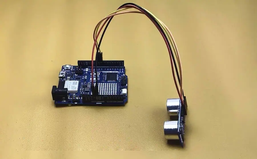 Arduino UNO R4 WiFi board connected to HC-SR04 ultrasonic sensor with red black yellow and brown jumper wires on yellow background
