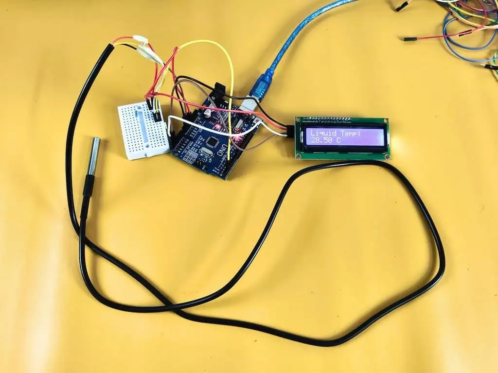 An Arduino Uno R3 breadboard circuit connecting a waterproof DS18B20 temperature sensor probe and an I2C LCD 1602 display showing a reading of 28.50 C.