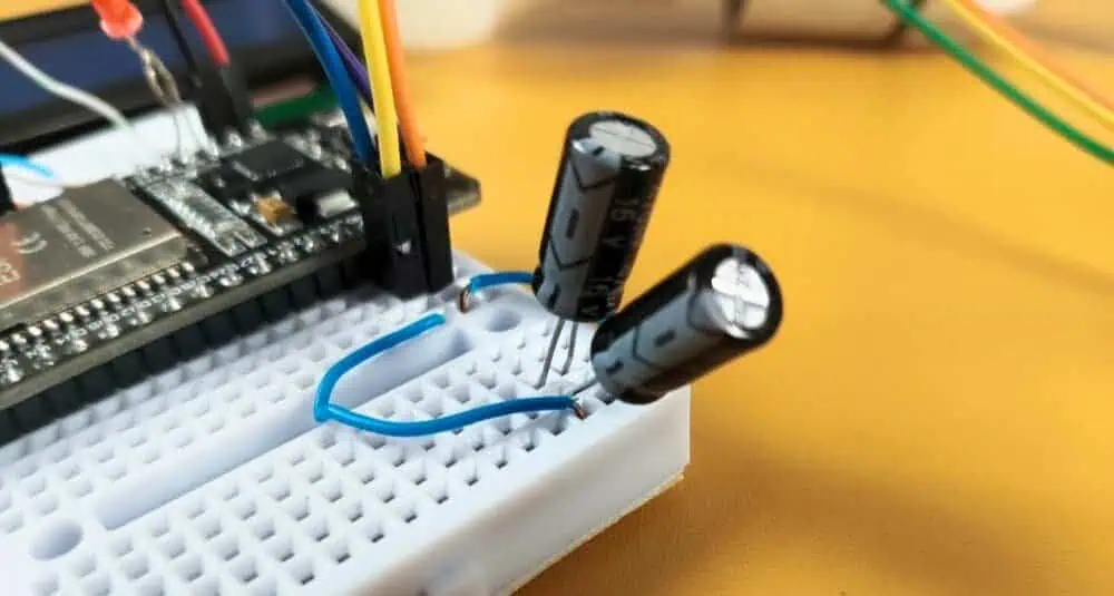 Two 470uF electrolytic capacitors connected in parallel on a breadboard next to an ESP32 to stabilize voltage and prevent I2C screen glitches.