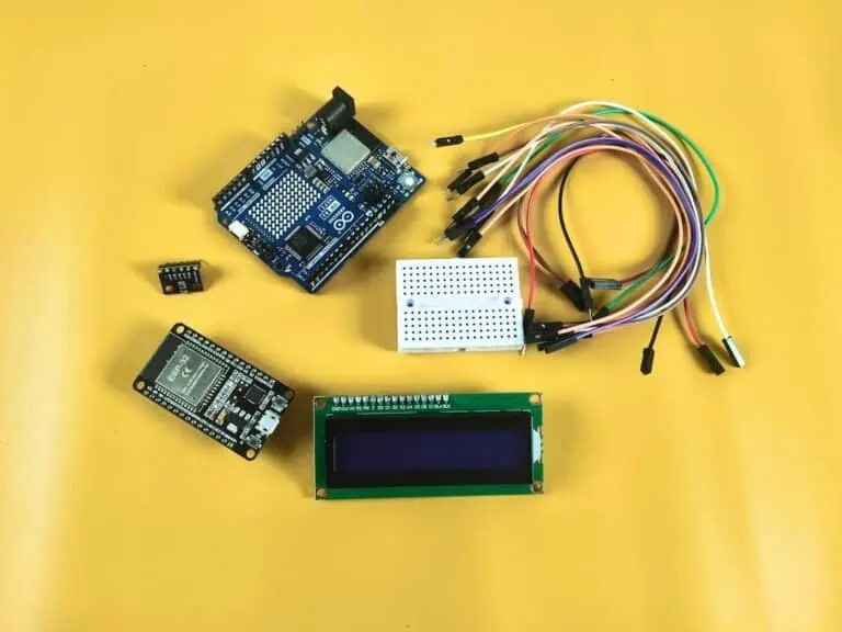 A high-quality comparison of an ESP32 board and an Arduino Uno R4 WiFi on a wooden desk, surrounded by a BMP280 sensor, LCD1602 display, and jumper wires for an IoT weather project.
