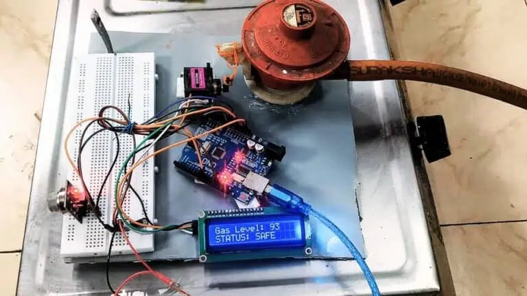 A completed Arduino-based smart LPG gas leakage detector project in action. The LCD screen shows a "SAFE" status with a gas level of 93, while the system is mounted next to a gas regulator on a stove.