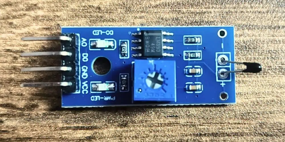 Close-up of a 10K thermistor temperature sensor module with VCC, GND, AO, and DO pins, LM393 comparator, adjustable potentiometer, and NTC thermistor.