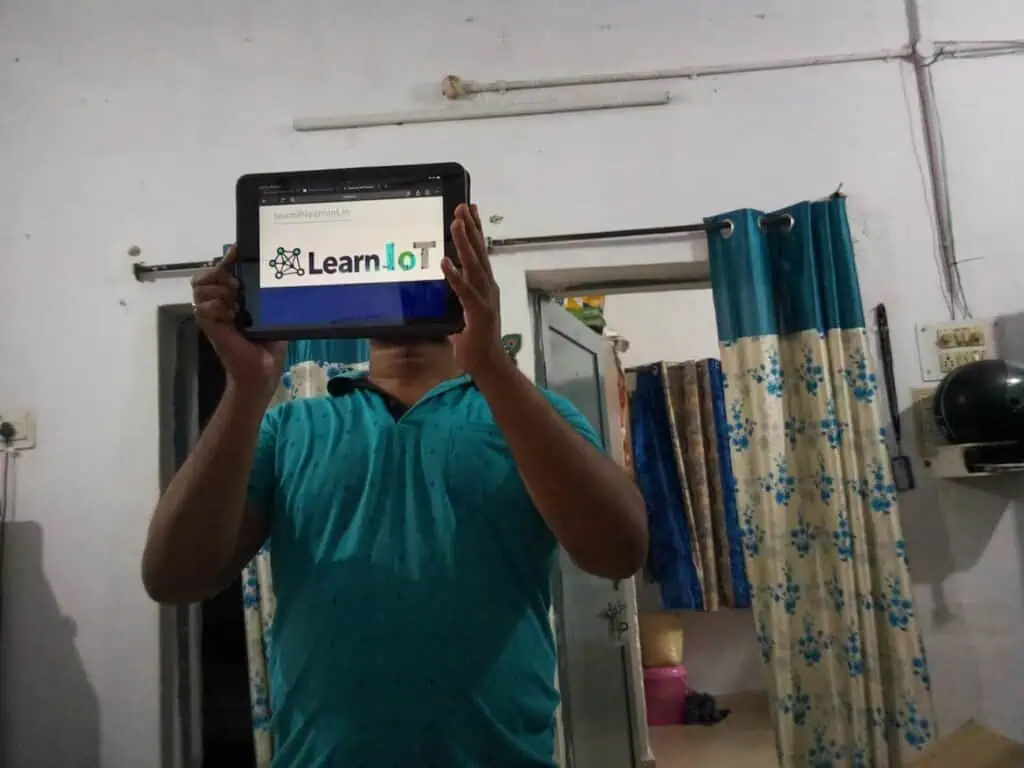 Indoor photo captured using the Raspberry Pi Camera Module showing a person holding a tablet displaying the LearnIoT website.